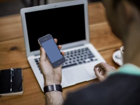Person holding a smartphone in front of an open laptop