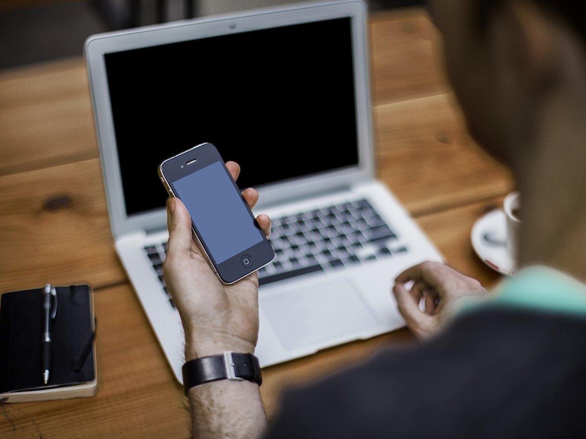 Person holding a smartphone in front of an open laptop